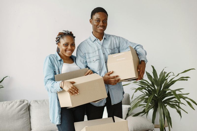 Young couple smiling and holding cardboard boxes while standing inside their new home.