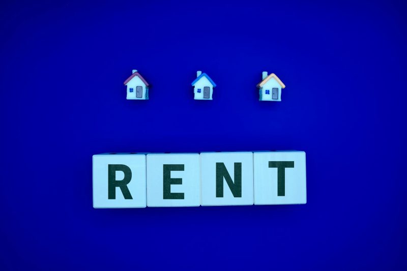 Miniature houses arranged above the letters spelling 'RENT' on a blue background.