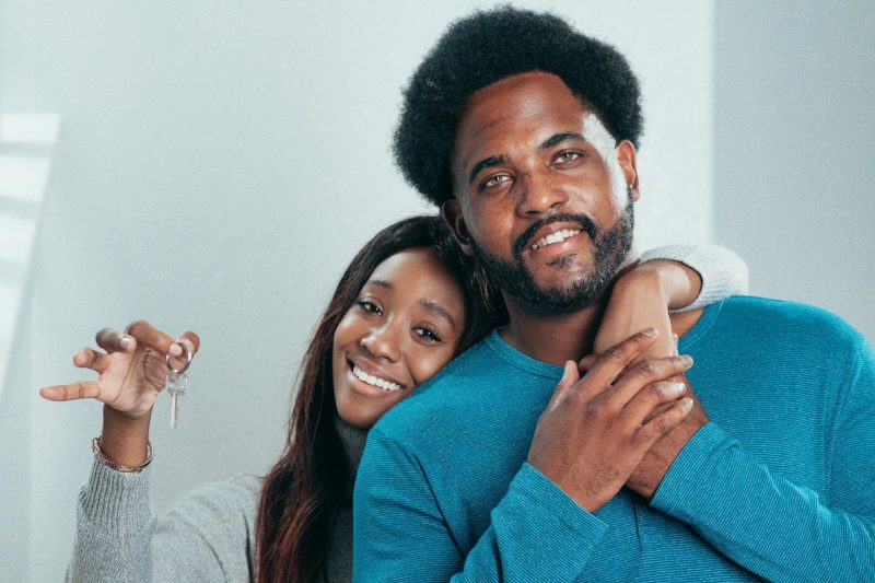 Joyful couple holding keys, standing outside a new home, smiling with excitement.