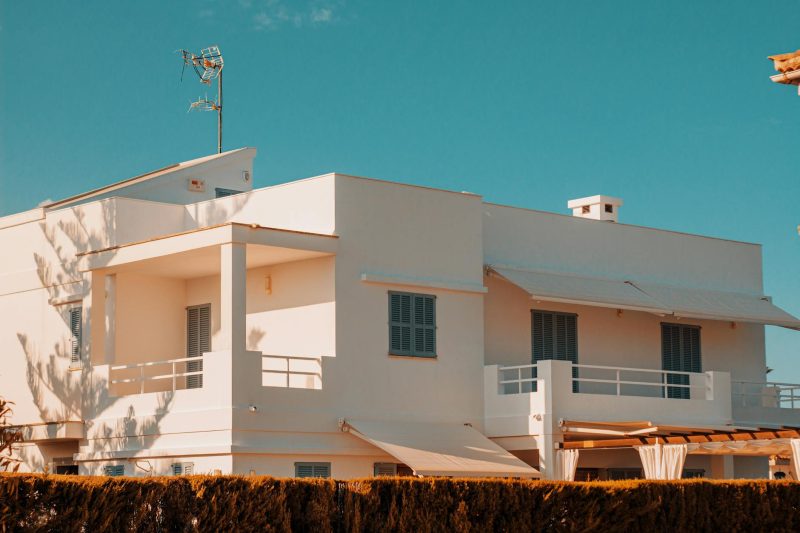 Elegant modern white house with balconies against a clear blue sky, featuring minimalistic architectural design.