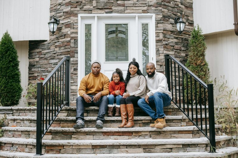 Young African American family, with a teenage boy and girl, sitting on a staircase and smiling at the camera.