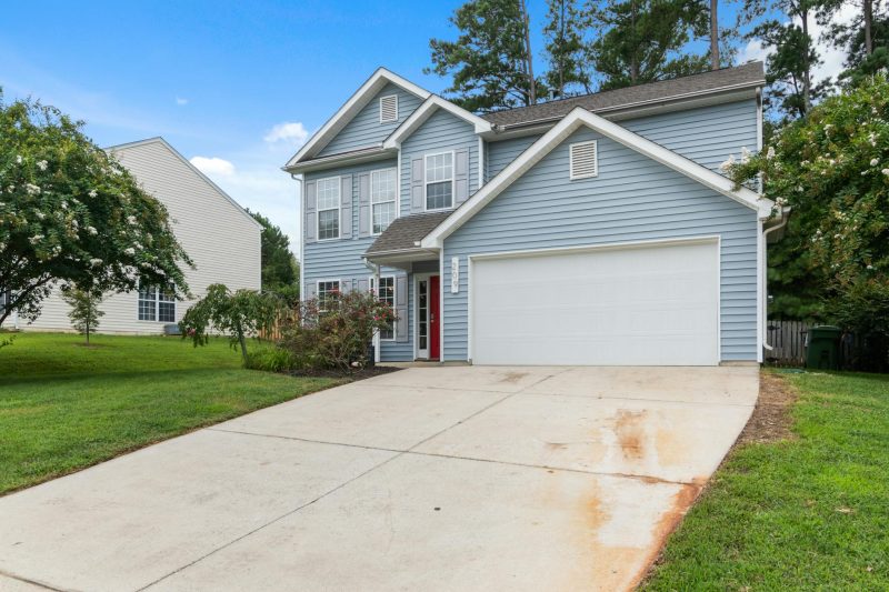 Charming two-story suburban house with a spacious driveway surrounded by lush greenery.