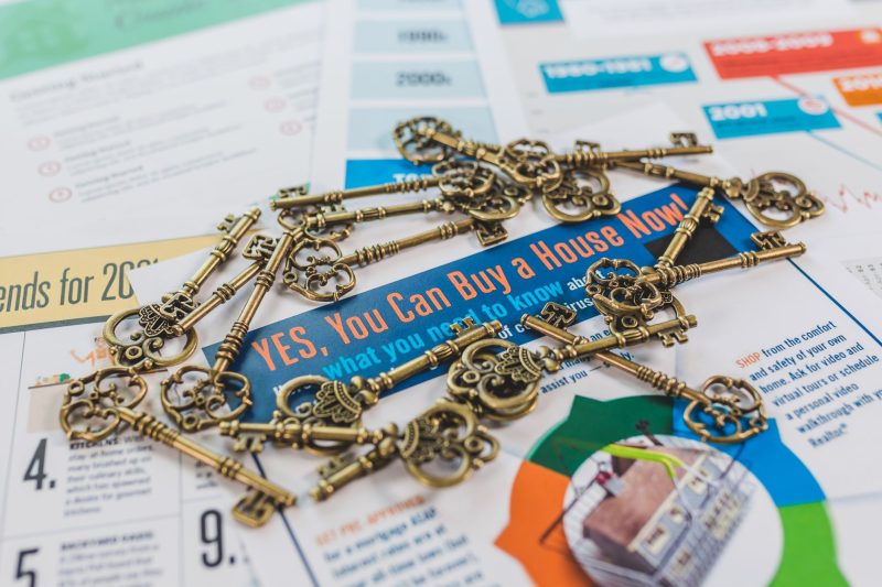 A collection of vintage keys arranged on a real estate brochure showcasing house buying options.