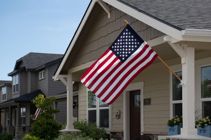 Stylish suburban house with a vibrant American flag displayed in front, surrounded by greenery.