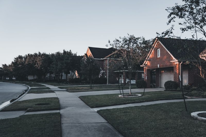 Serene suburban scene with brick houses and manicured lawns under a dusky sky.