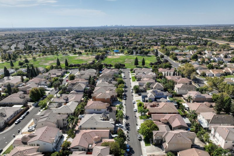 Aerial view of a Sacramento suburb featuring rows of houses and abundant greenery under clear blue skies.